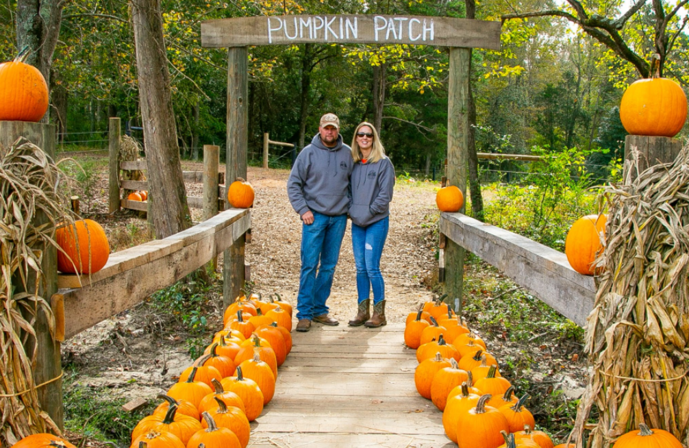 Man and woman standing in front of pumpkin patch sign 